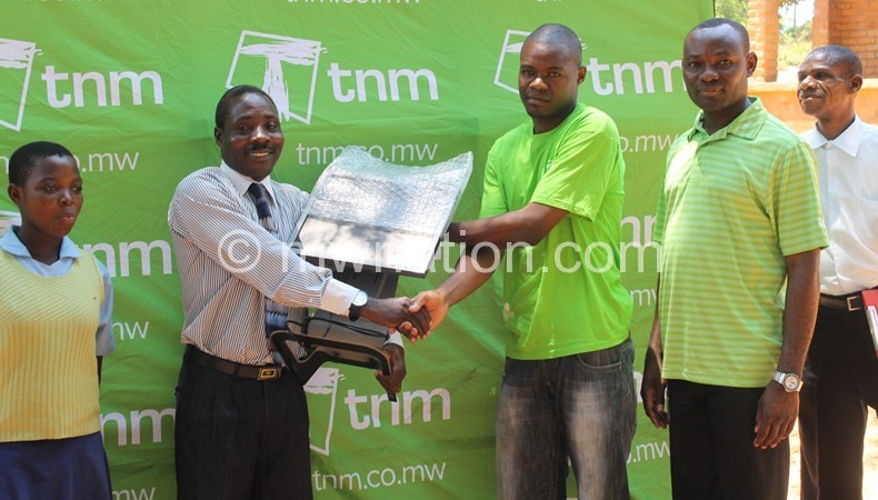 Francis Chilowa [TNM winner] presenting one of computers to the headmaster of Chintheche CDSS Eston Kaponde and looking on is TNM Head of region North Richard Kwatiwani [in green golf shirt].