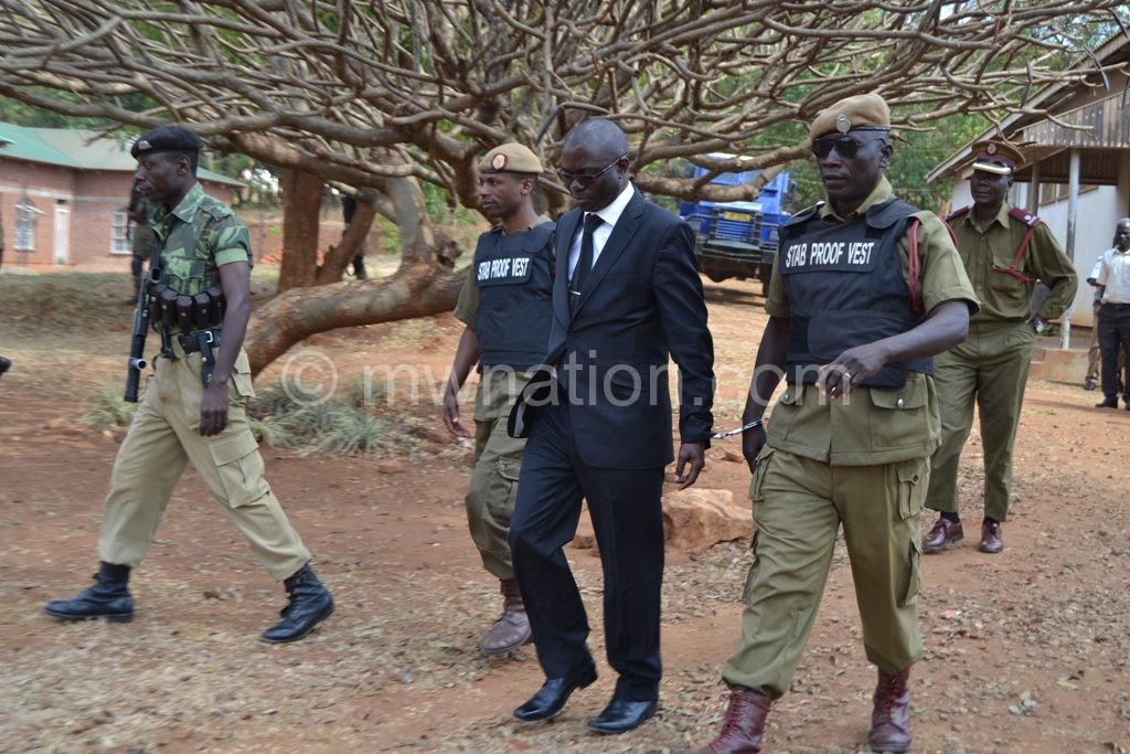 Kasambara (in suit) captured in police escort during the trial period   