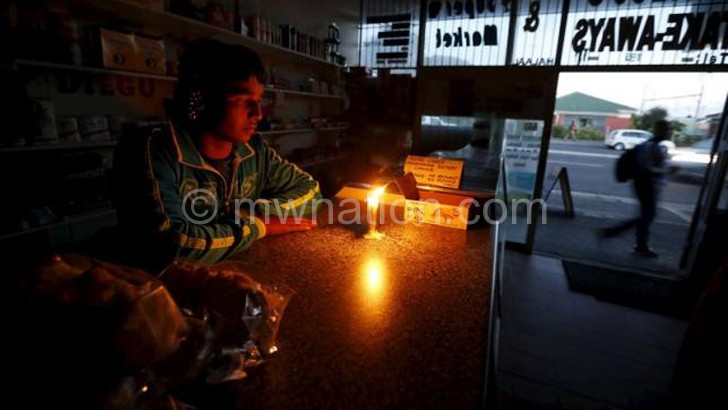 A shopkeeper waits for customers in his candlelit fast food store during a blackout in Capetown