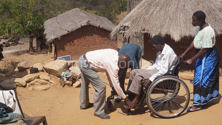 Community health workers assist a patient (in wheelchair) in a Neno village