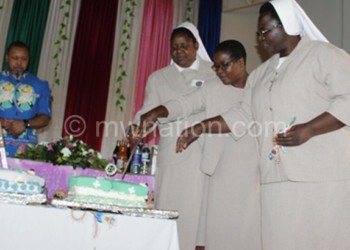 The sisters cut a cake as Chilima looks on