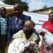 Changole (in blue suit) donates a blanket to an elderly woman as other officials look on