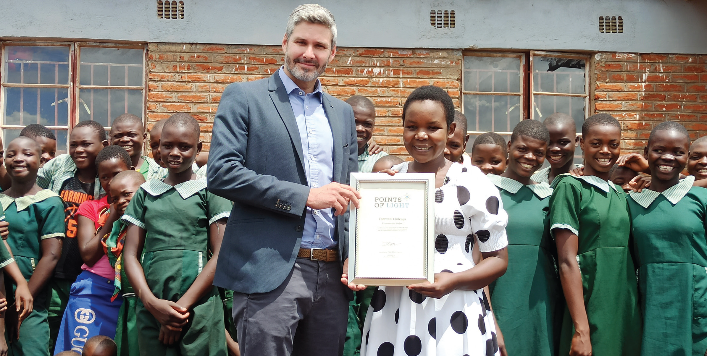 Beer (L) presents the Queen’s award to Temwani alongside pupils