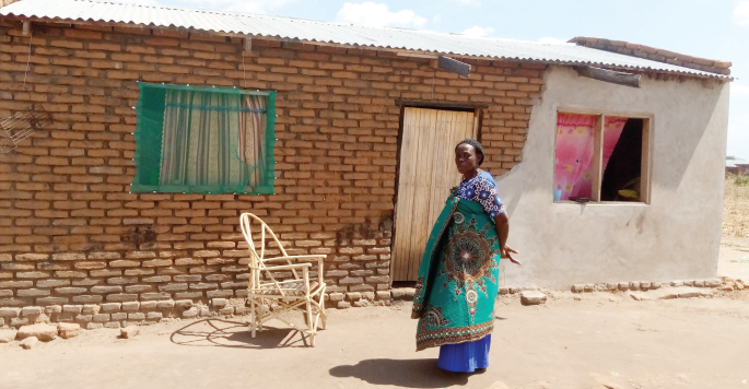 Ndovie standing infront of her house she built with money from the programme